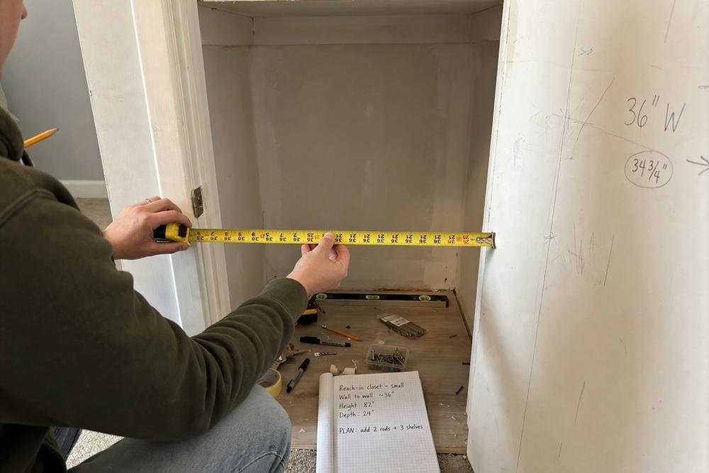 Measuring a small reach in closet with a tape measure before adding rods and shelves
