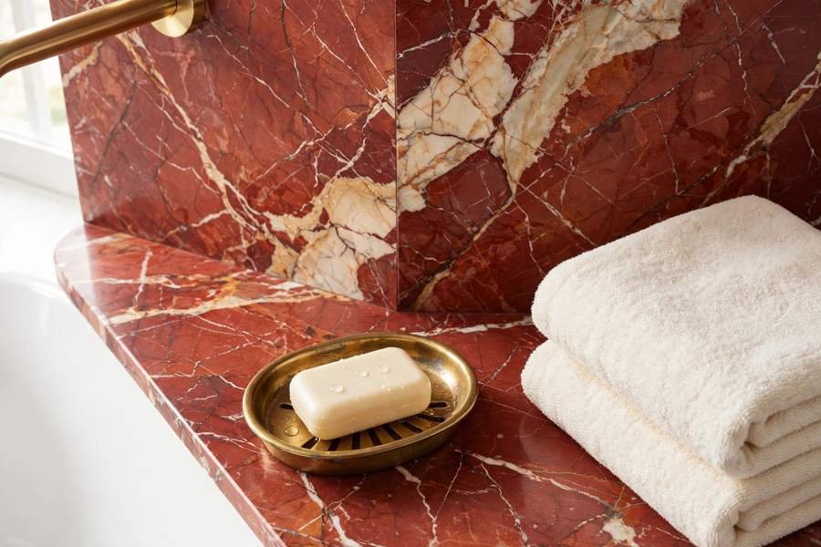 Red marble bathroom detail with veining, a brass soap dish and cream towels